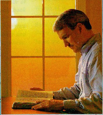 man reading a Bible near a window